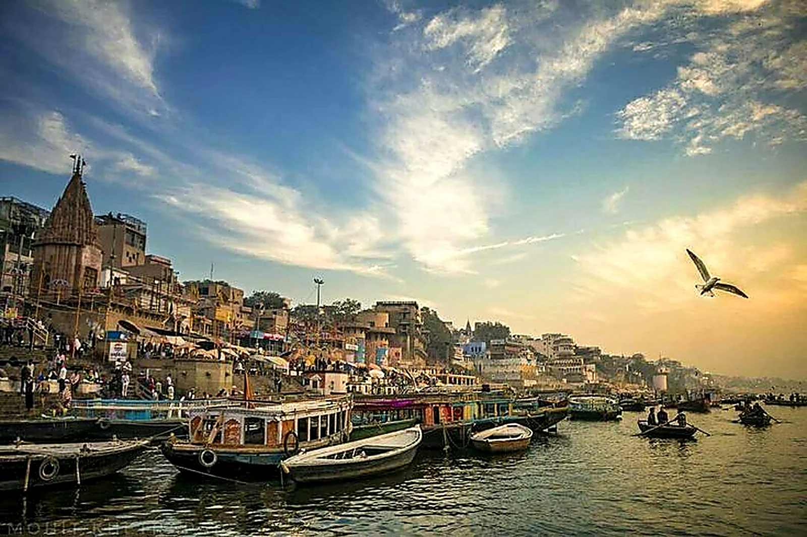 Wooden boats moored along the ghats of Varanasi at sunrise with temples rising behind the riverbank